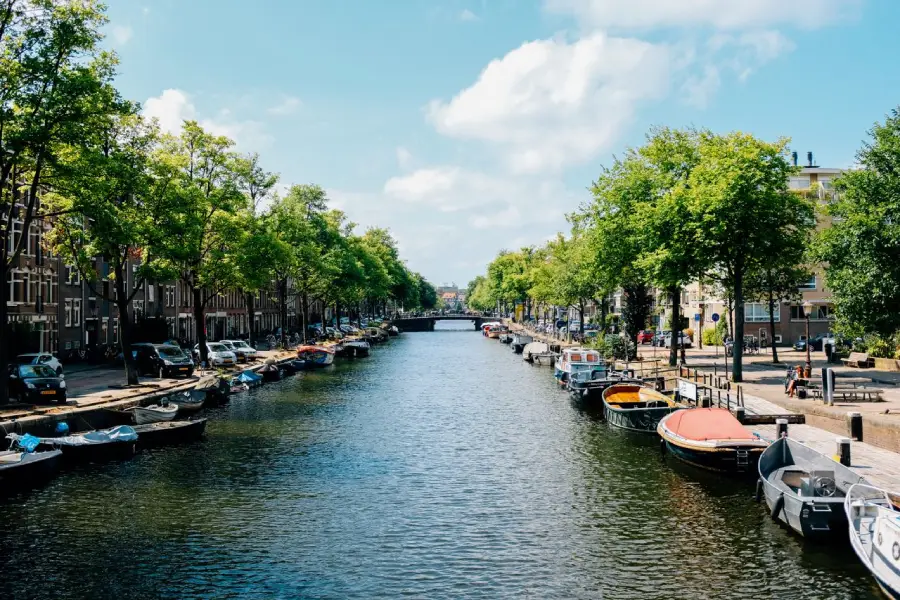 Canal de Amsterdã cercado por barcos, árvores e prédios 